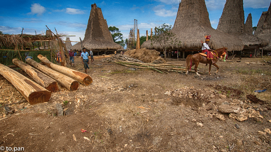 A horseman riding passes four main pillars of mayela wood quality that are laid on ground in a queue to be erected